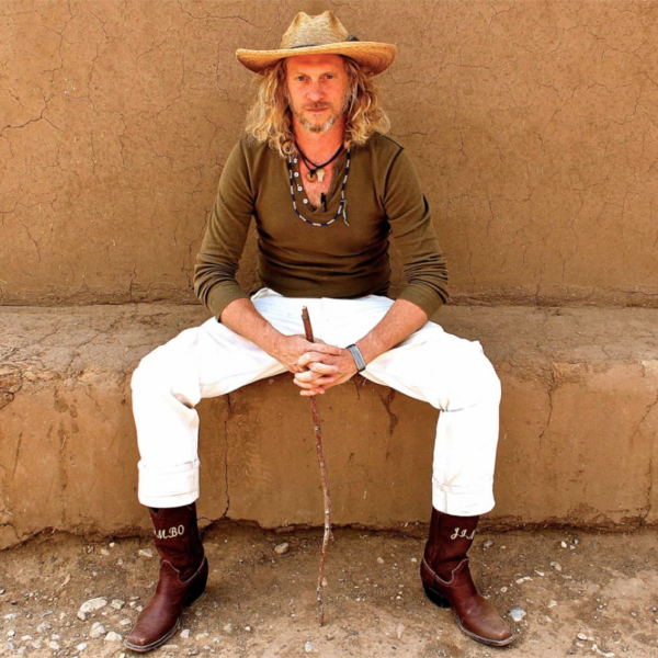 Jimbo Mathus wears a straw hat and sits on a bench.
