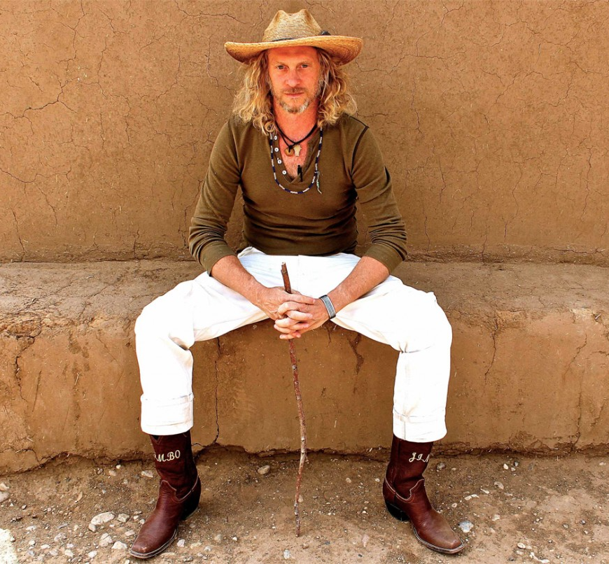 Jimbo Mathus wears a straw hat and sits on a bench.