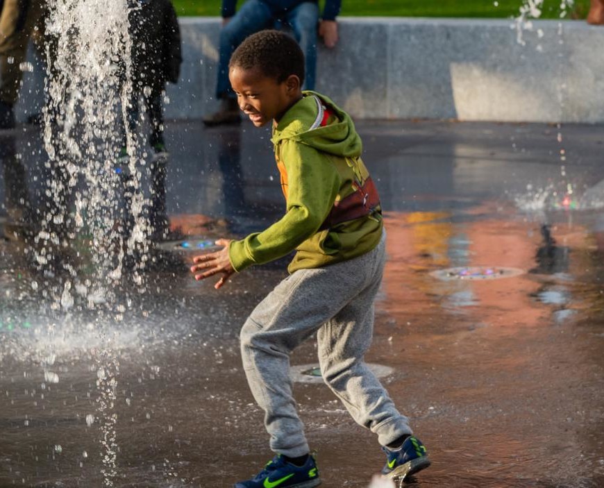 A child plays in the City Hall Park splash pad fountain.