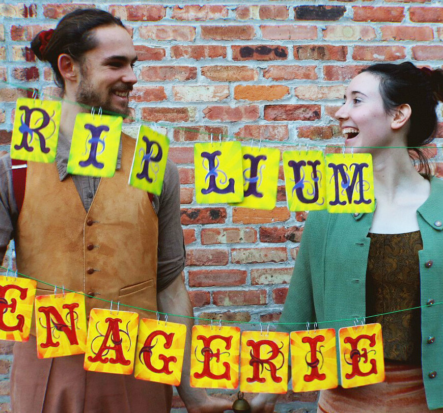 A light skinned woman and man hold an elaborate hand lettered sign that says Riplium Menagerie