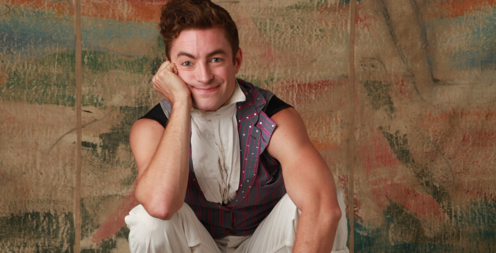 A circus performer balances on a board and smiles at the camera.