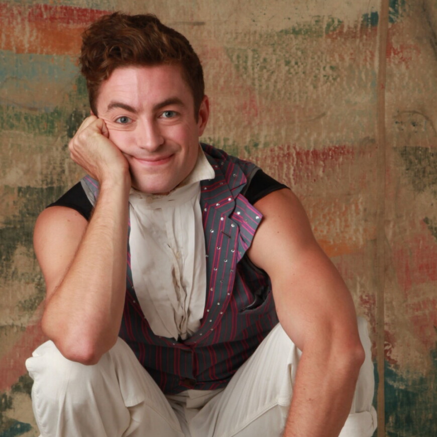 A circus performer balances on a board and smiles at the camera.